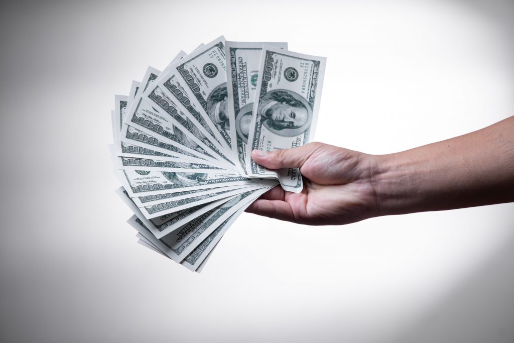 A hand holding several 100 dollar bills